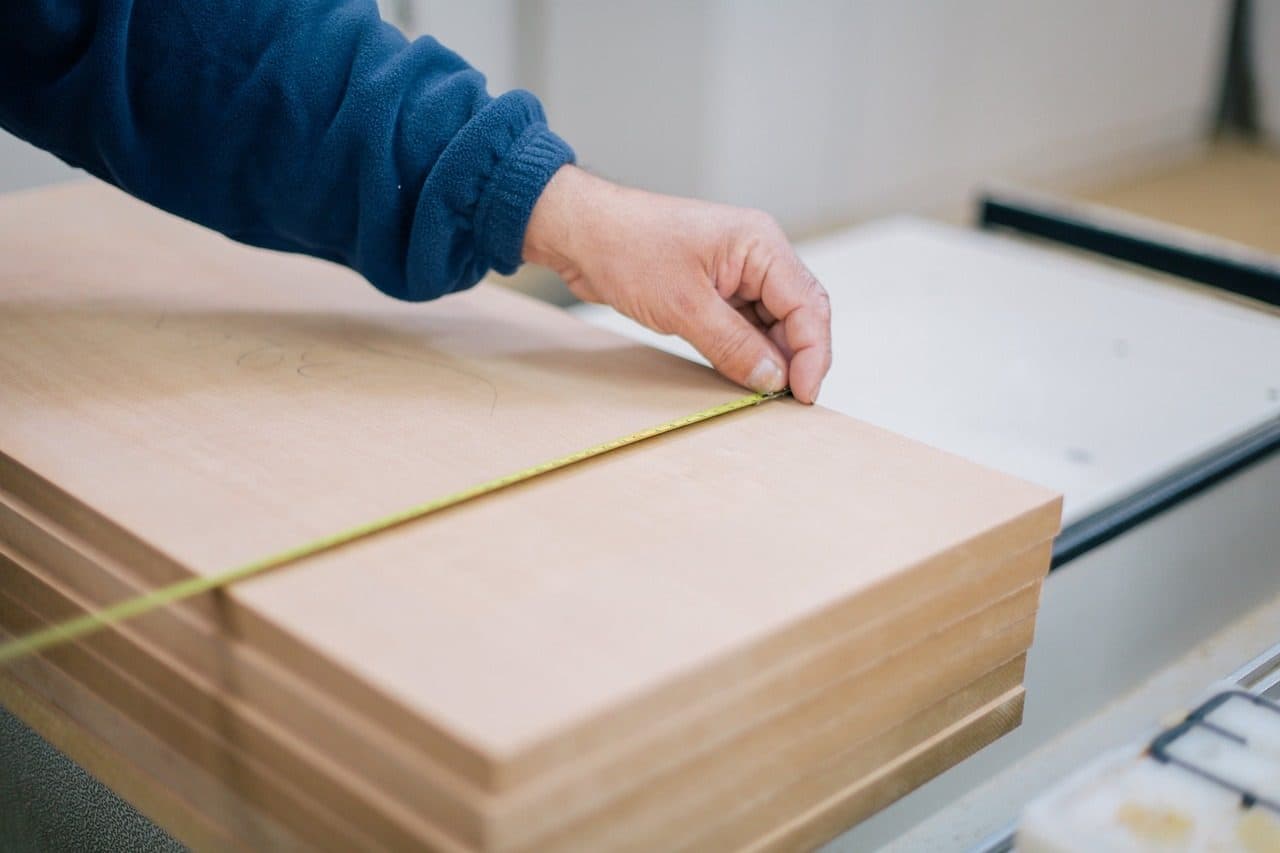 Hands measuring a panel on a CNC saw, because a marketing plan only works when you measure it