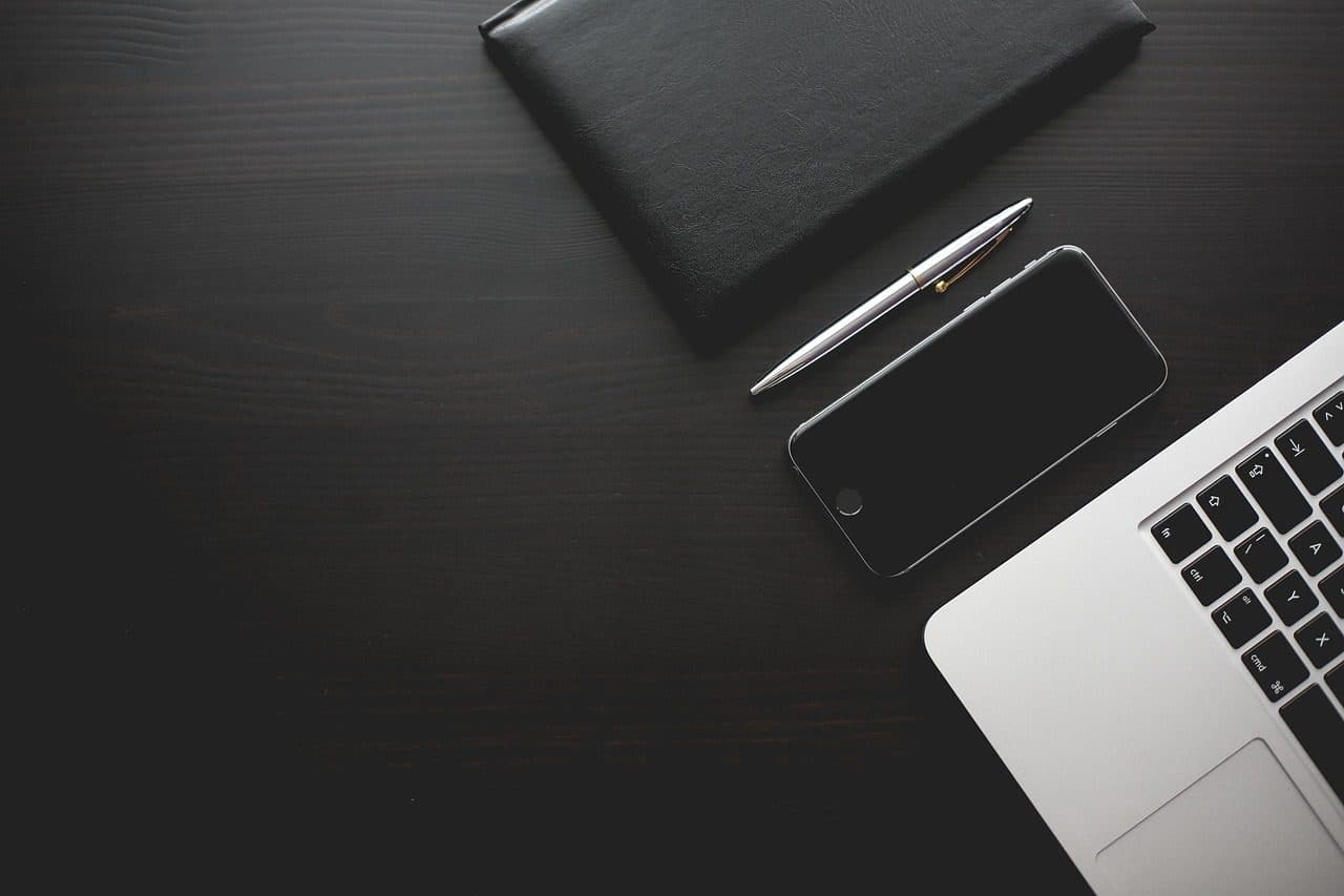 Smartphone and notebook on a dark office desk, ready for a fast reply to a new enquiry