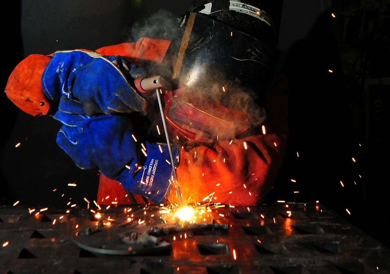 Welder in protective gear working through a shower of sparks, the kind of skilled work a strategy should put in front of buyers